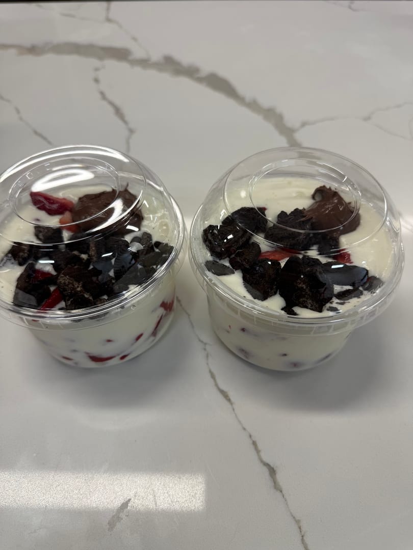 Two plastic cups of creamy dessert with strawberries, chocolate chunks, and chocolate spread.