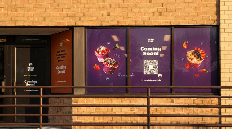 Pura Vida restaurant's "Coming Soon!" signs on a brick building, featuring açai bowls and a QR code.