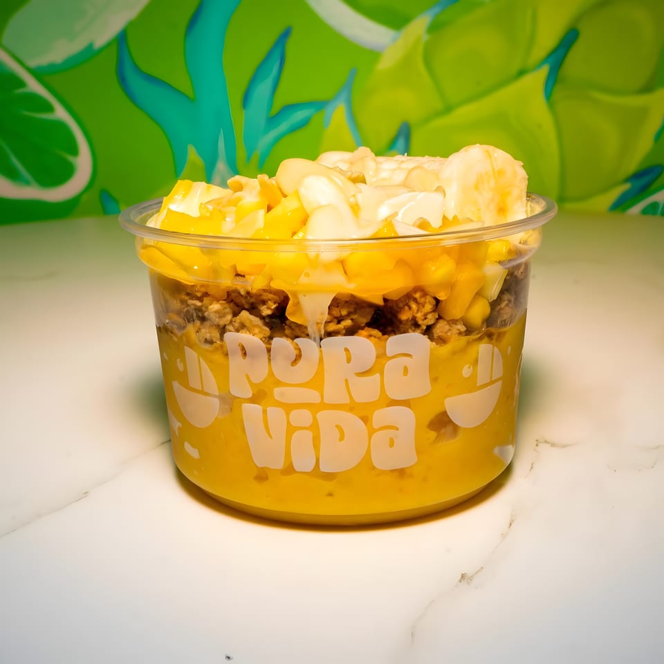 Pura Vida mango smoothie bowl with granola, banana, and coconut flakes on a marble counter.