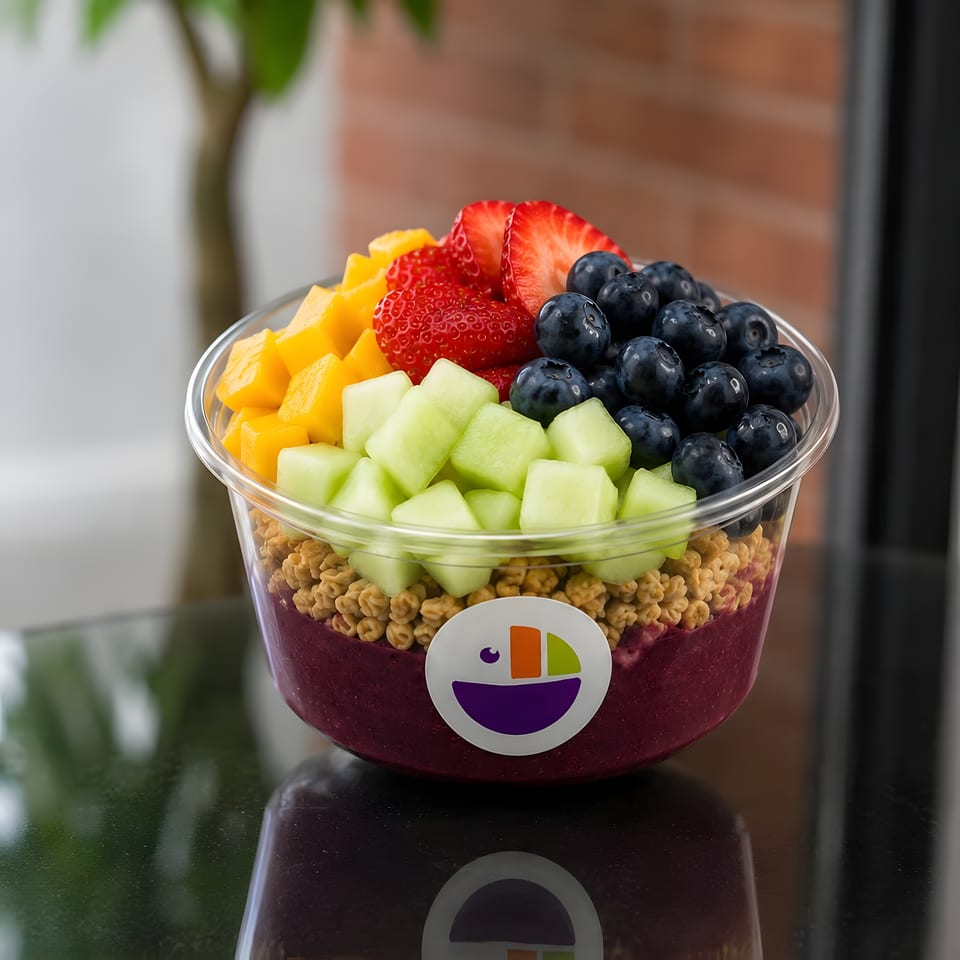 A colorful acai bowl with mango, strawberries, blueberries, and honeydew, topped with granola.