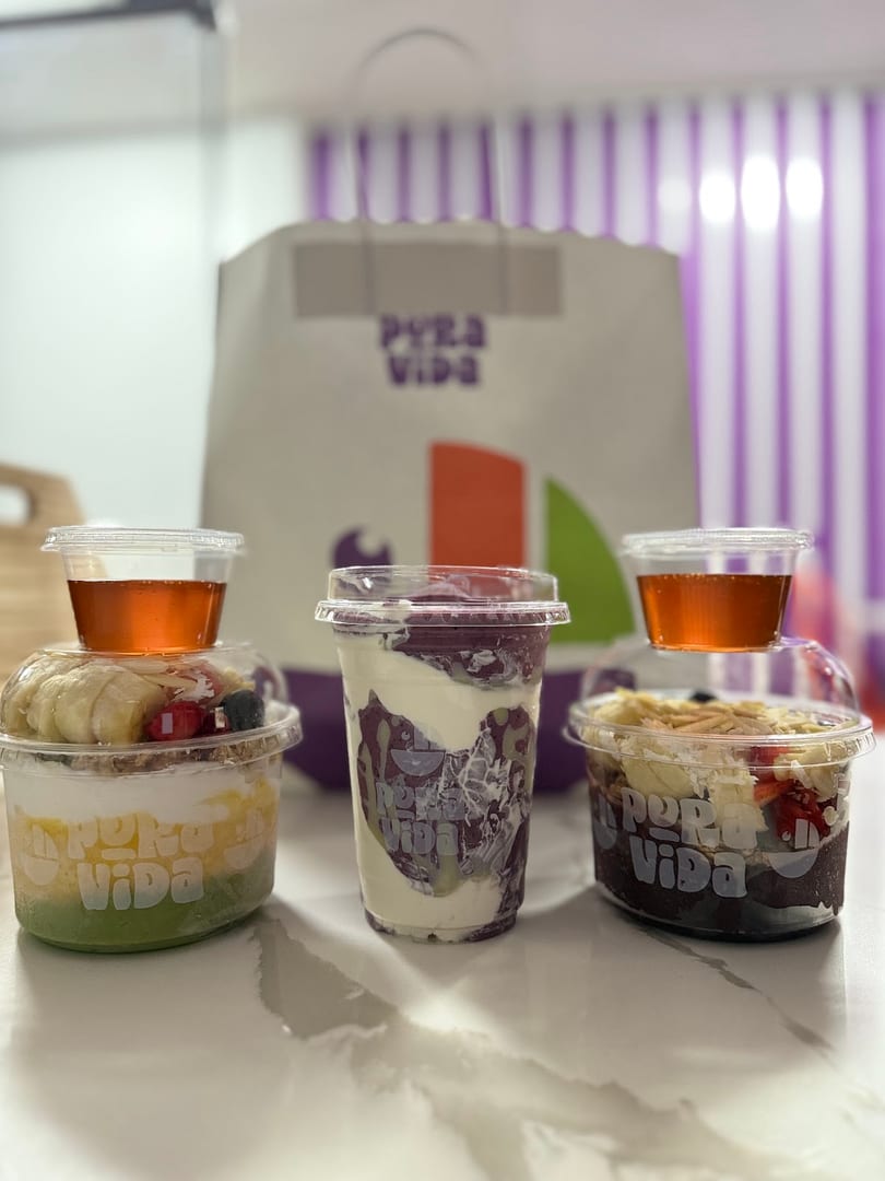 Three Pura Vida layered fruit and yogurt bowls with syrup, in front of a branded bag.